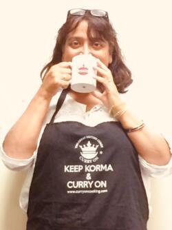 Spice Sister Veena Josh wearting a black apron and drinking from